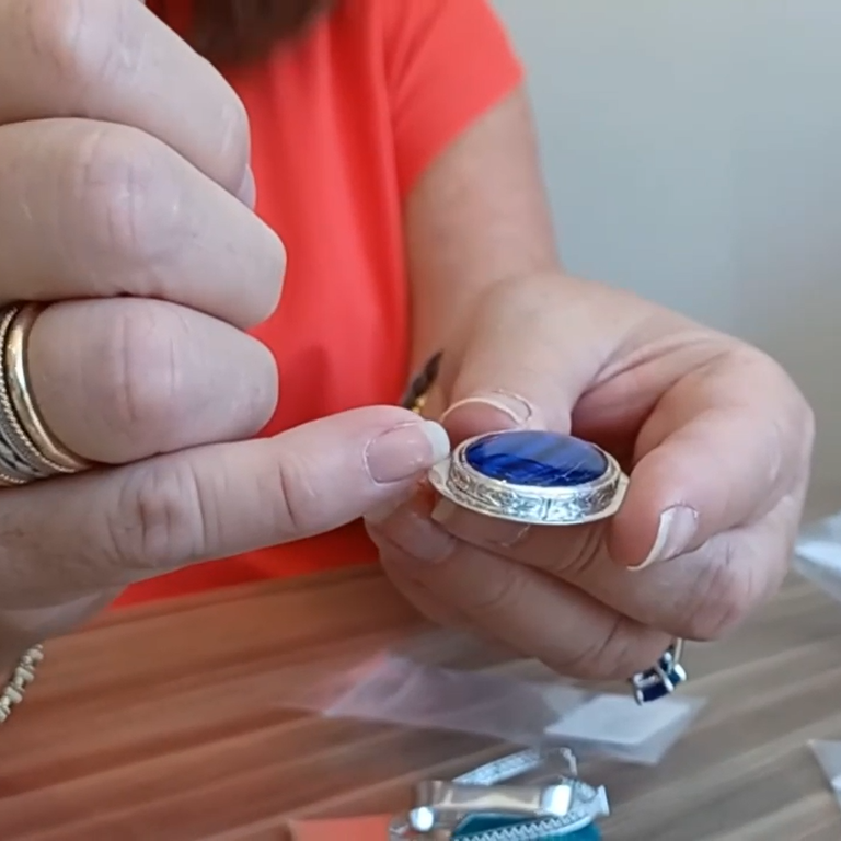 Jeweler holding a blue gemstone in a silver bezel setting with jewelry making supplies in the background